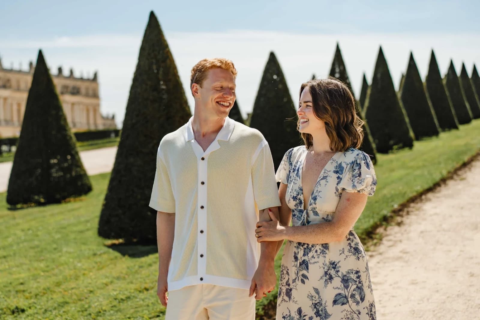 Joyful couple laughing in the gardens of the Palace of Versailles near Paris during a romantic engagement session by SabShots