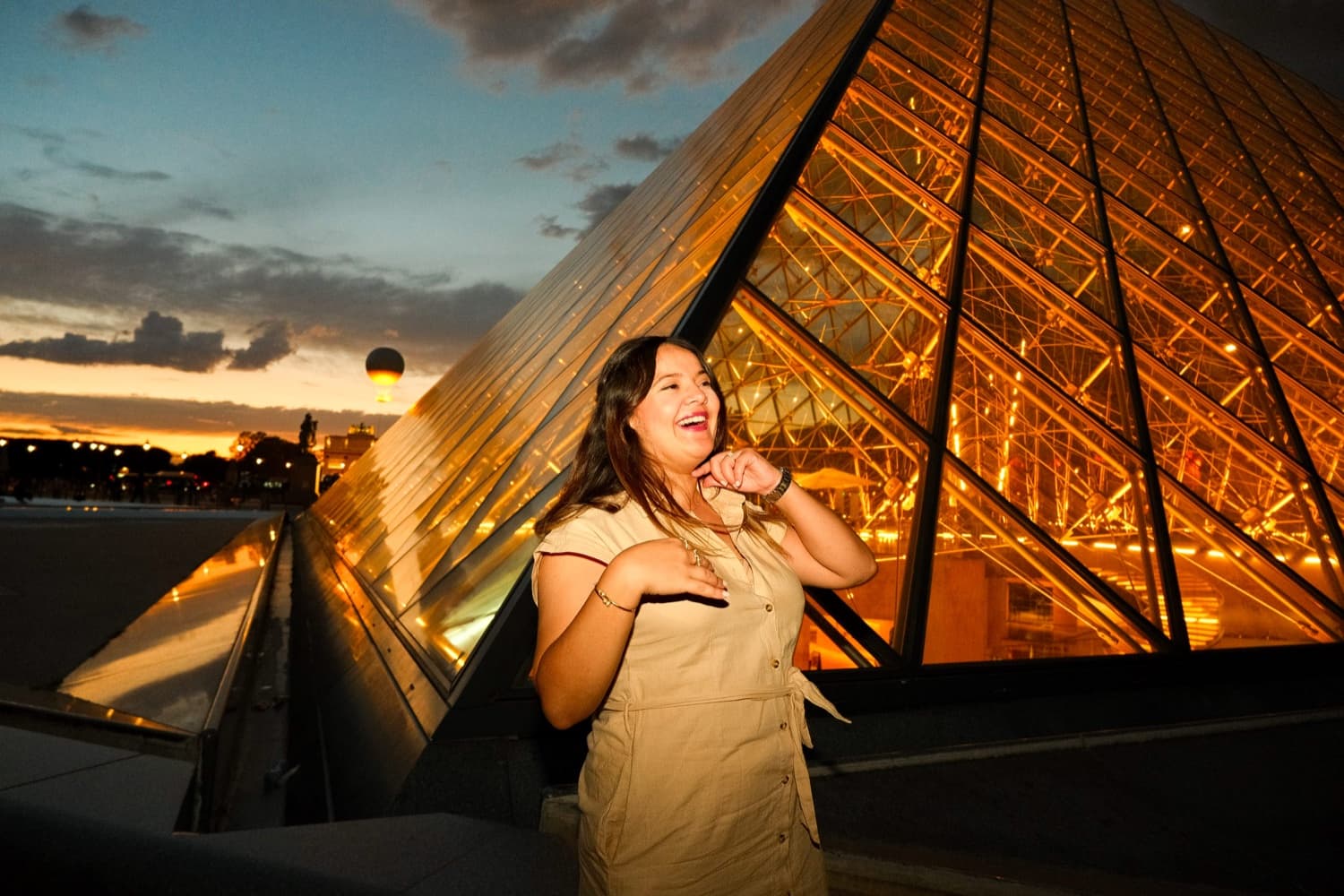 Woman laughing beside the glowing Louvre Pyramid at sunset in Paris by SabShots