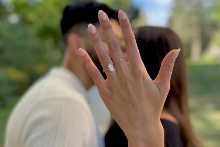 Close-up of a diamond engagement ring as a newly engaged couple kisses, a Paris surprise proposal by SabShots